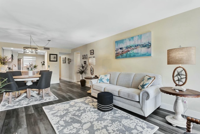 living room with dark wood-style floors, baseboards, visible vents, and an inviting chandelier