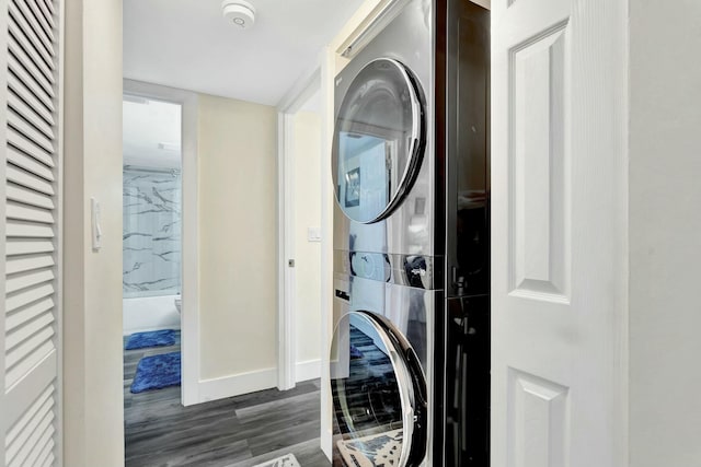 laundry room featuring stacked washer and dryer, baseboards, laundry area, and wood finished floors