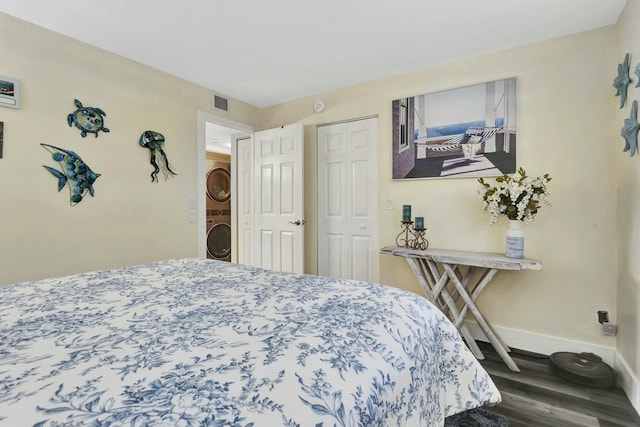 bedroom featuring a closet, visible vents, stacked washing maching and dryer, wood finished floors, and baseboards