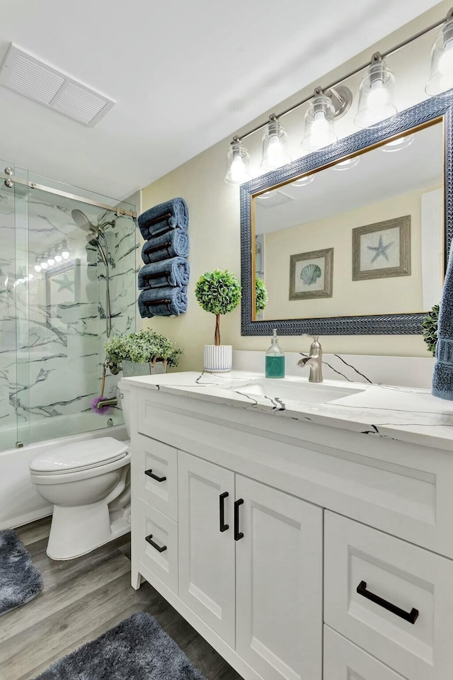 full bathroom featuring toilet, wood finished floors, vanity, visible vents, and combined bath / shower with glass door