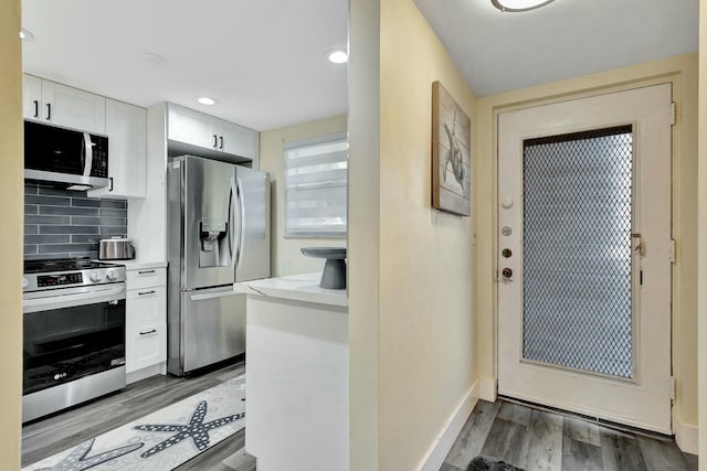 kitchen featuring stainless steel appliances, light countertops, decorative backsplash, white cabinets, and wood finished floors