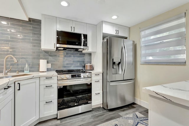 kitchen featuring tasteful backsplash, appliances with stainless steel finishes, white cabinets, a sink, and light wood-type flooring