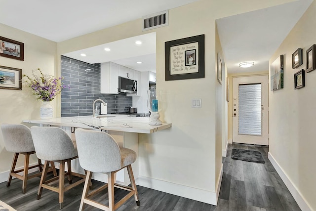 kitchen featuring a breakfast bar, tasteful backsplash, stainless steel microwave, visible vents, and a peninsula