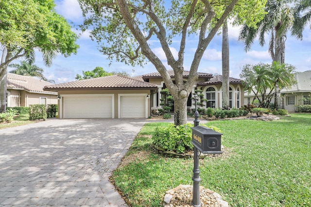 mediterranean / spanish house with decorative driveway, stucco siding, an attached garage, a tiled roof, and a front lawn