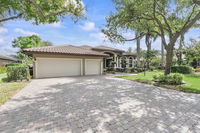 mediterranean / spanish-style home featuring a tiled roof, an attached garage, decorative driveway, a front yard, and stucco siding