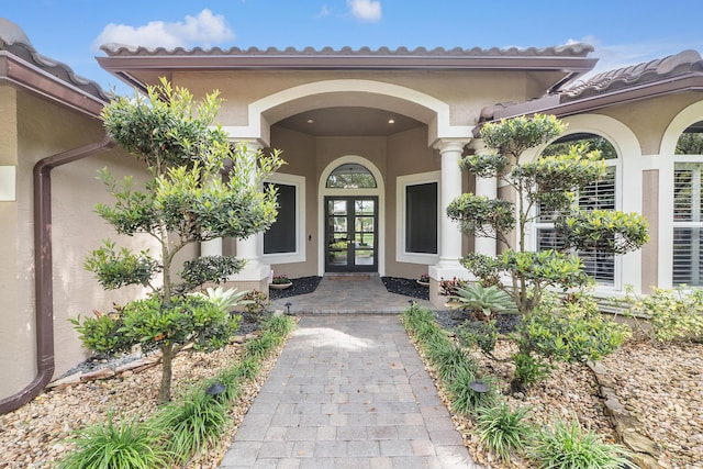 property entrance with stucco siding, a tiled roof, and french doors