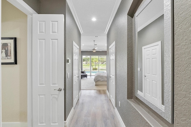 corridor featuring light wood finished floors, ornamental molding, and a textured wall