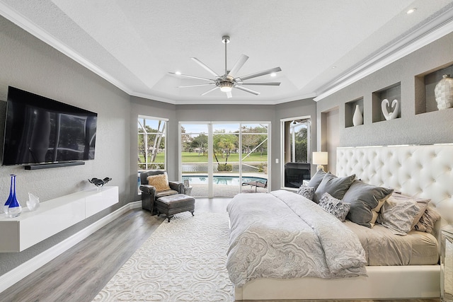 bedroom featuring access to exterior, a tray ceiling, ornamental molding, and wood finished floors