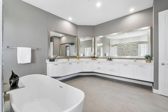 bathroom featuring double vanity, a freestanding tub, a sink, and recessed lighting