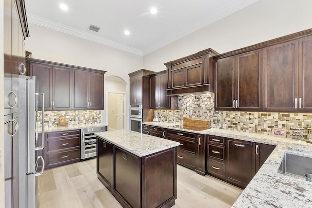 kitchen with arched walkways, wine cooler, stainless steel appliances, a kitchen island, and visible vents