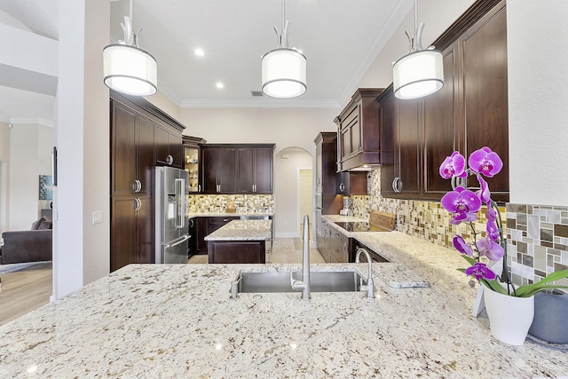 kitchen with high end refrigerator, arched walkways, light stone counters, crown molding, and a sink