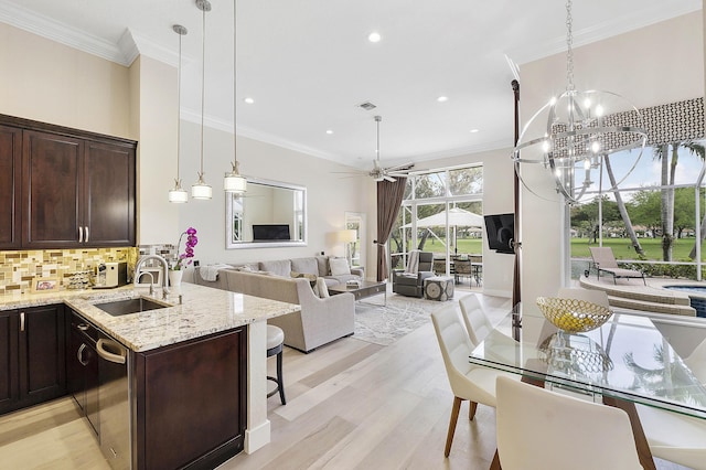 kitchen featuring backsplash, ornamental molding, a sink, dark brown cabinets, and light stone countertops