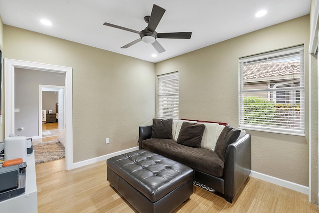 living area featuring ceiling fan, light wood-type flooring, and baseboards