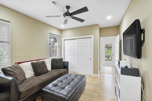 living room featuring plenty of natural light, light wood-style flooring, ceiling fan, and a textured wall