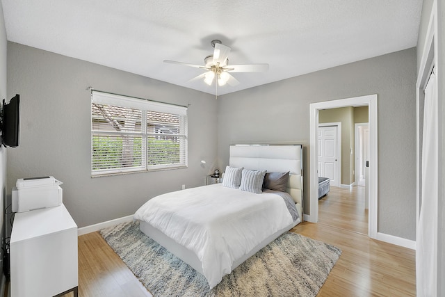 bedroom with ceiling fan, a textured wall, light wood-style flooring, and baseboards