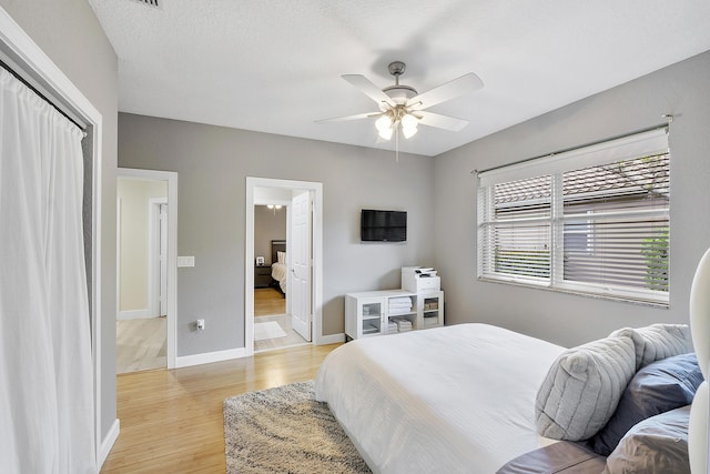 bedroom with baseboards, ceiling fan, a textured ceiling, and light wood finished floors