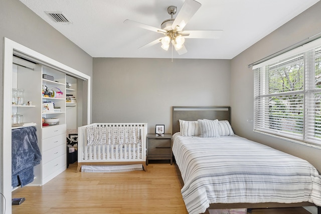 bedroom with light wood-type flooring, ceiling fan, visible vents, and a closet