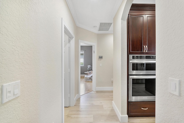 corridor featuring ornamental molding, a textured wall, light wood-style flooring, and visible vents