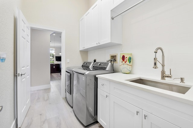 laundry room with a sink, baseboards, light wood-type flooring, cabinet space, and washing machine and clothes dryer