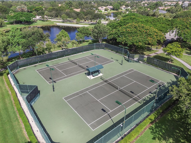 view of tennis court with a water view and fence