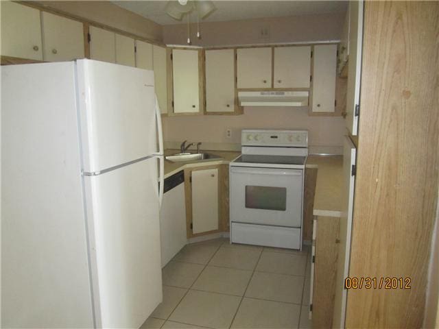 kitchen featuring white appliances, light tile patterned floors, a sink, light countertops, and under cabinet range hood