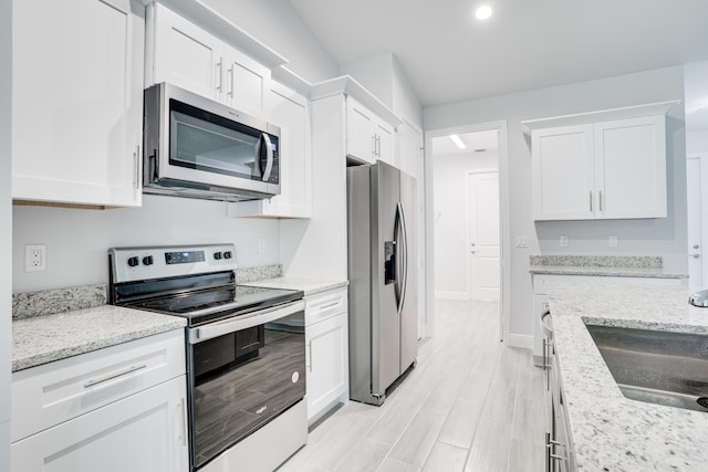 kitchen featuring appliances with stainless steel finishes, a sink, light stone counters, and white cabinets