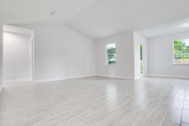 empty room featuring lofted ceiling, baseboards, visible vents, and a wealth of natural light