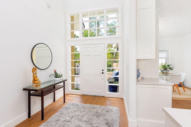 foyer entrance with baseboards, light wood-type flooring, and ornamental molding