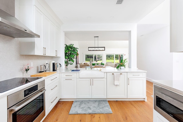 kitchen featuring light wood finished floors, a sink, stainless steel appliances, white cabinetry, and wall chimney exhaust hood