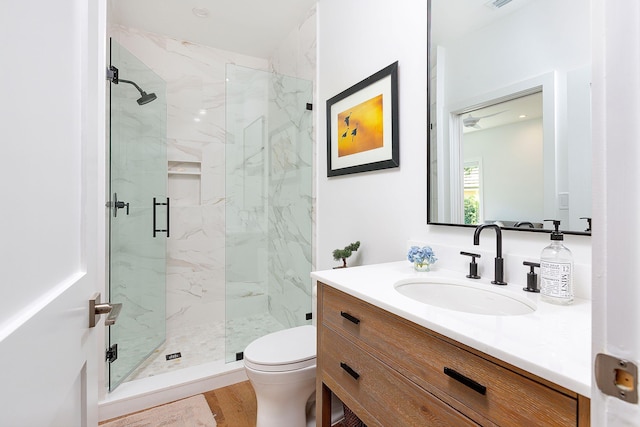 bathroom featuring a marble finish shower, toilet, vanity, and wood finished floors