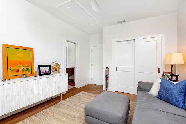 living area featuring attic access, wood finished floors, visible vents, and baseboards