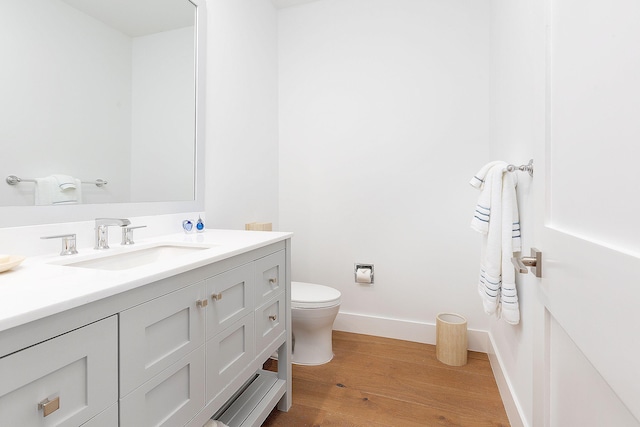 bathroom with toilet, vanity, baseboards, and wood finished floors