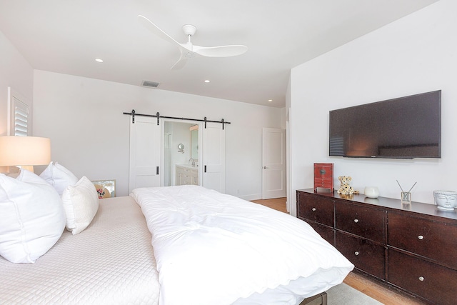 bedroom with a ceiling fan, visible vents, ensuite bath, light wood-style floors, and a barn door