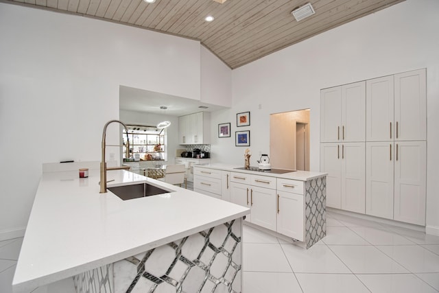 kitchen with a sink, a peninsula, white cabinets, light tile patterned floors, and wood ceiling