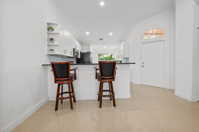 kitchen with a peninsula, white cabinetry, freestanding refrigerator, open shelves, and stainless steel microwave