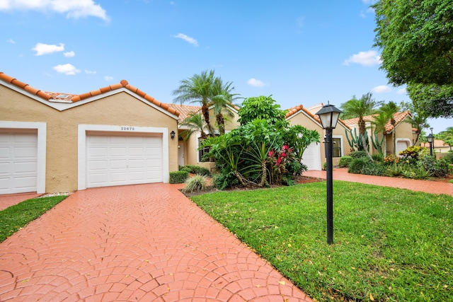 view of front of house featuring an attached garage, a tiled roof, decorative driveway, stucco siding, and a front lawn