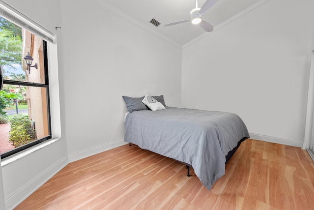 bedroom with baseboards, light wood-type flooring, visible vents, and crown molding