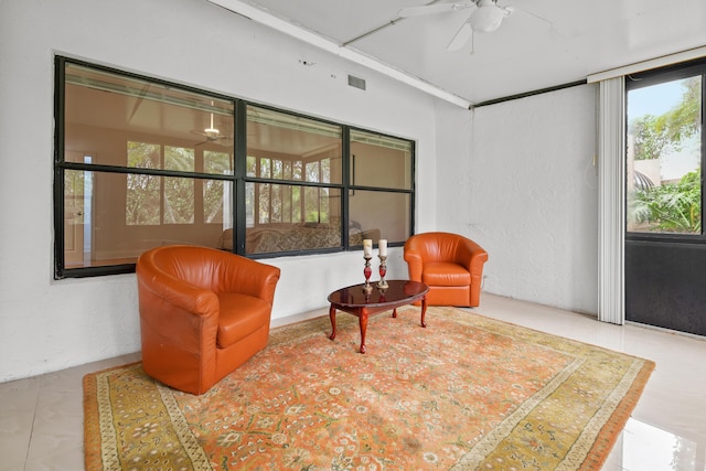 living area featuring a sunroom, visible vents, a ceiling fan, and a textured wall