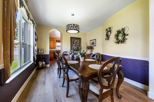 dining area with wood finished floors, arched walkways, and baseboards