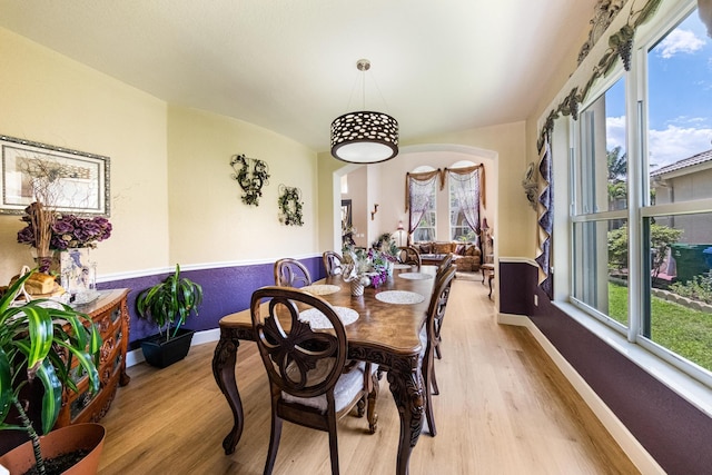 dining room featuring baseboards, arched walkways, and light wood finished floors