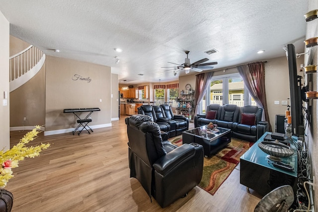 living room featuring visible vents, baseboards, a textured ceiling, and light wood finished floors