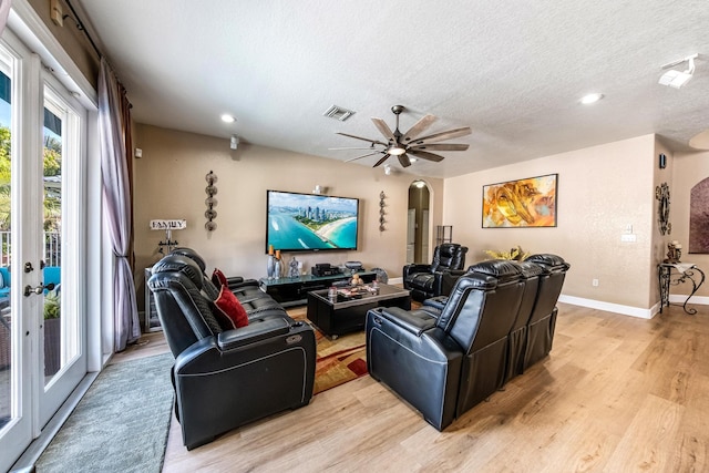 living room featuring visible vents, a textured ceiling, arched walkways, light wood finished floors, and ceiling fan