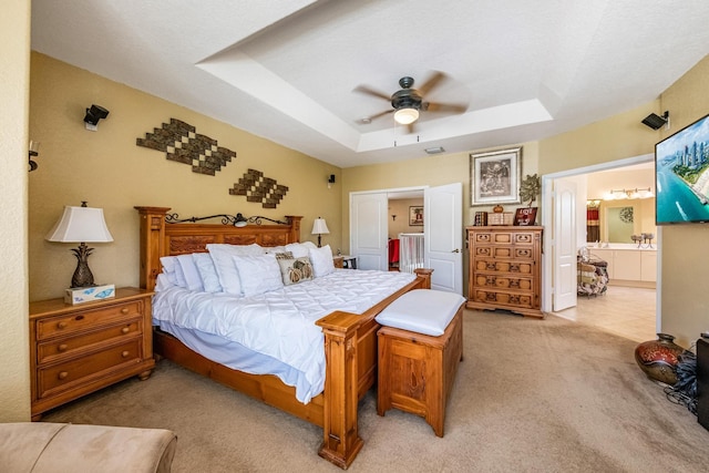 bedroom with ceiling fan, a raised ceiling, connected bathroom, and light carpet