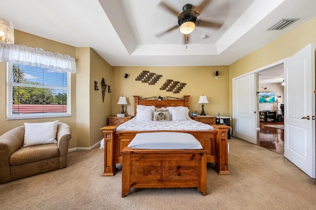 bedroom featuring visible vents, baseboards, a tray ceiling, ceiling fan, and light colored carpet