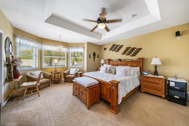 bedroom with baseboards, ceiling fan, light colored carpet, a tray ceiling, and a textured ceiling