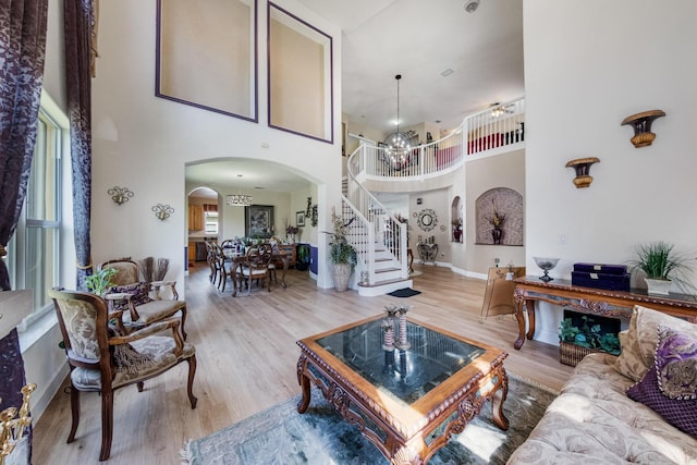 living room featuring wood finished floors, an inviting chandelier, arched walkways, stairs, and a towering ceiling