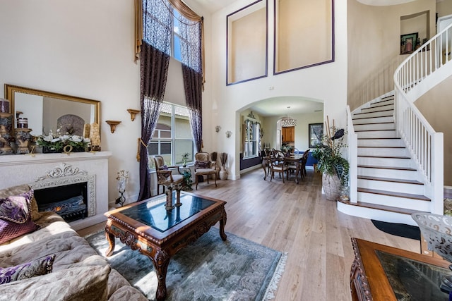 living area featuring stairway, baseboards, light wood-style flooring, arched walkways, and a lit fireplace