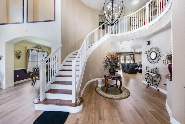 stairway featuring baseboards, ceiling fan with notable chandelier, a towering ceiling, wood finished floors, and arched walkways