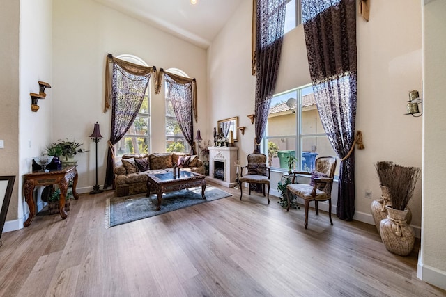 sitting room with a fireplace with raised hearth, baseboards, a towering ceiling, and wood finished floors