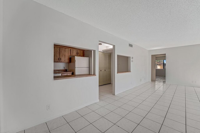 empty room featuring visible vents, a textured ceiling, and light tile patterned flooring